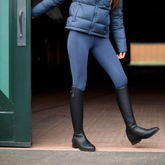 Person wearing blue riding tights and black boots stepping out of a barn.